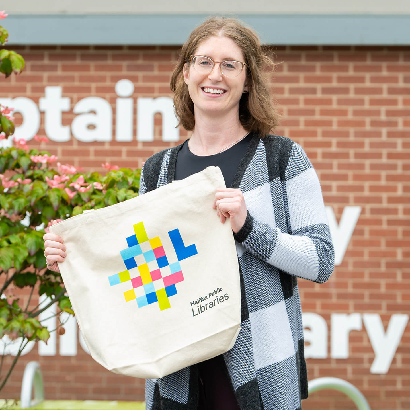 Danielle holding up a Library branded tote bag, smiling to camera.